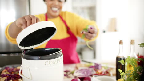 African American woman adds vegetable scraps to a compost bin in a bright kitchen at home