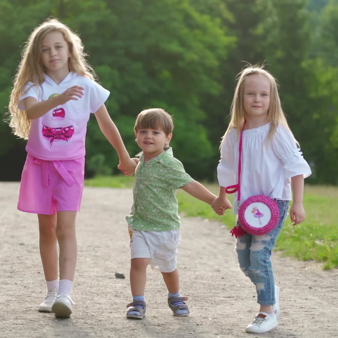 Two girls and one boy walk happily on the ground road in park. Sisters and brother have family day outdoor in summer. Concept video