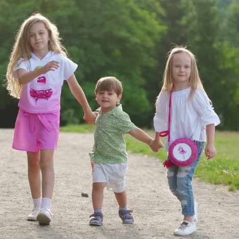 two girls and one boy walk happily on the ground road in park. sisters and brother have family day outdoor in summer. concept video
