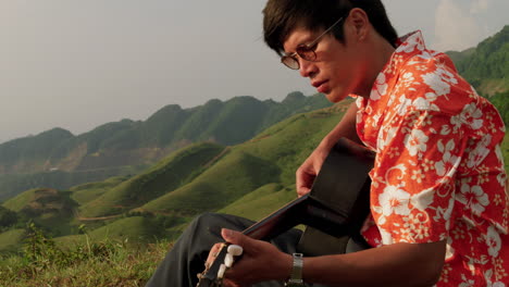 Asian-guy-playing-guitar-at-mountain-in-Vietnam,-closeup-slow-motion