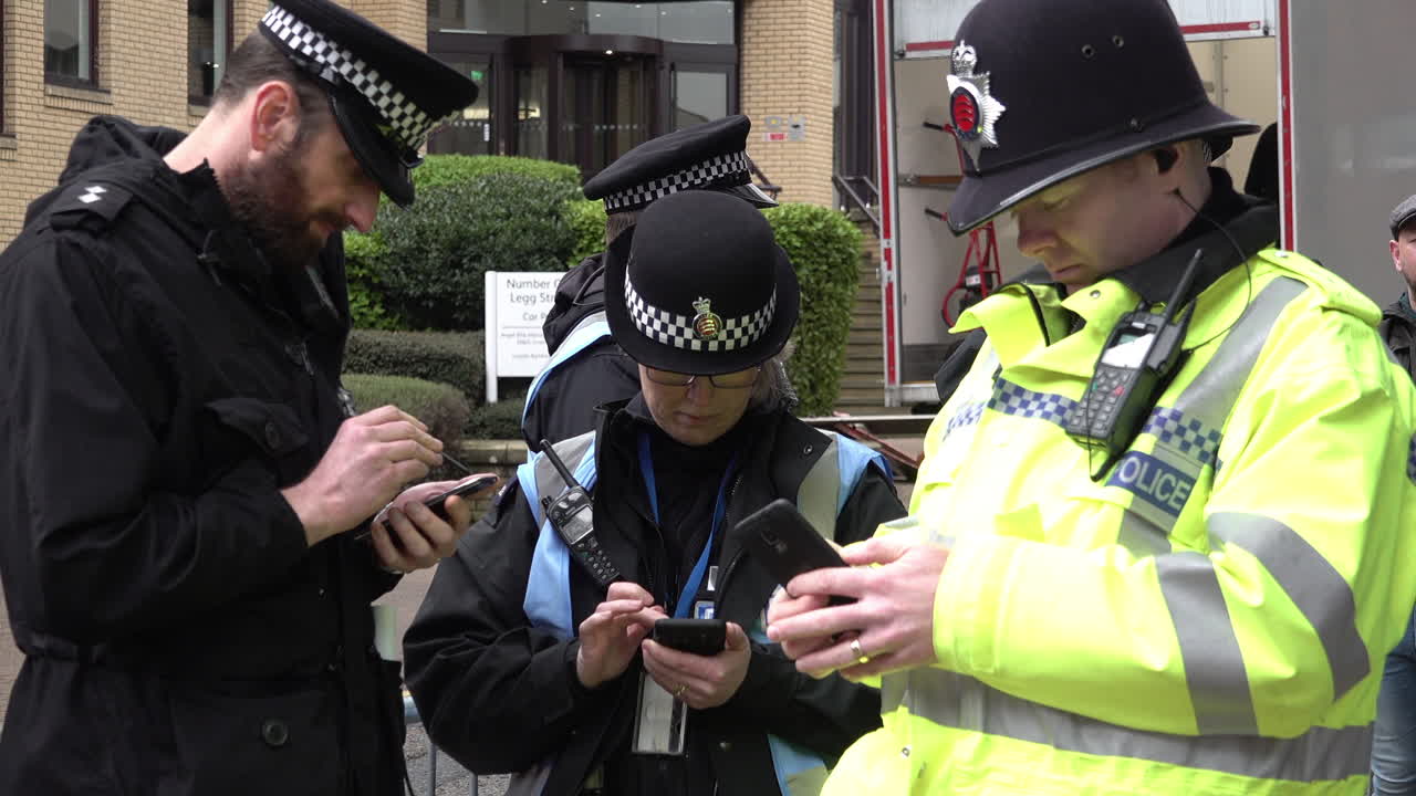 UK February 2019 - Police officers stand in a group tapping using mobile phones.