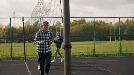 sports enthusiasts running on sports court, coach visible in background, all dressed in sportswear, focus on their movement as they participate in outdoor physical training session