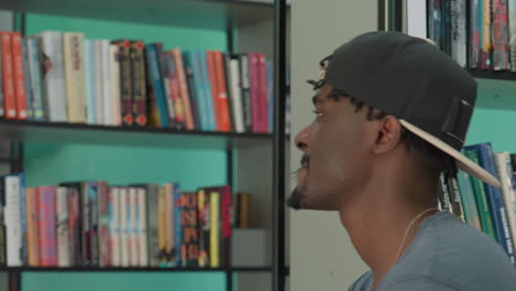 close up of young man in cap dancing in study room near books, side profile by shelves, relaxed mood, rhythm, casual style, academic setting, confident energy, learning vibe, under soft light