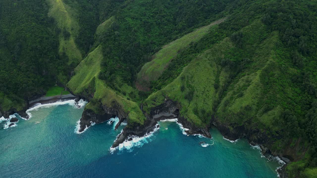 Advancing aerial of Dingalan, Aurora, pushing forward over lush green cliffs and rugged coves as turquoise waters crash against the shoreline under a partly cloudy sky