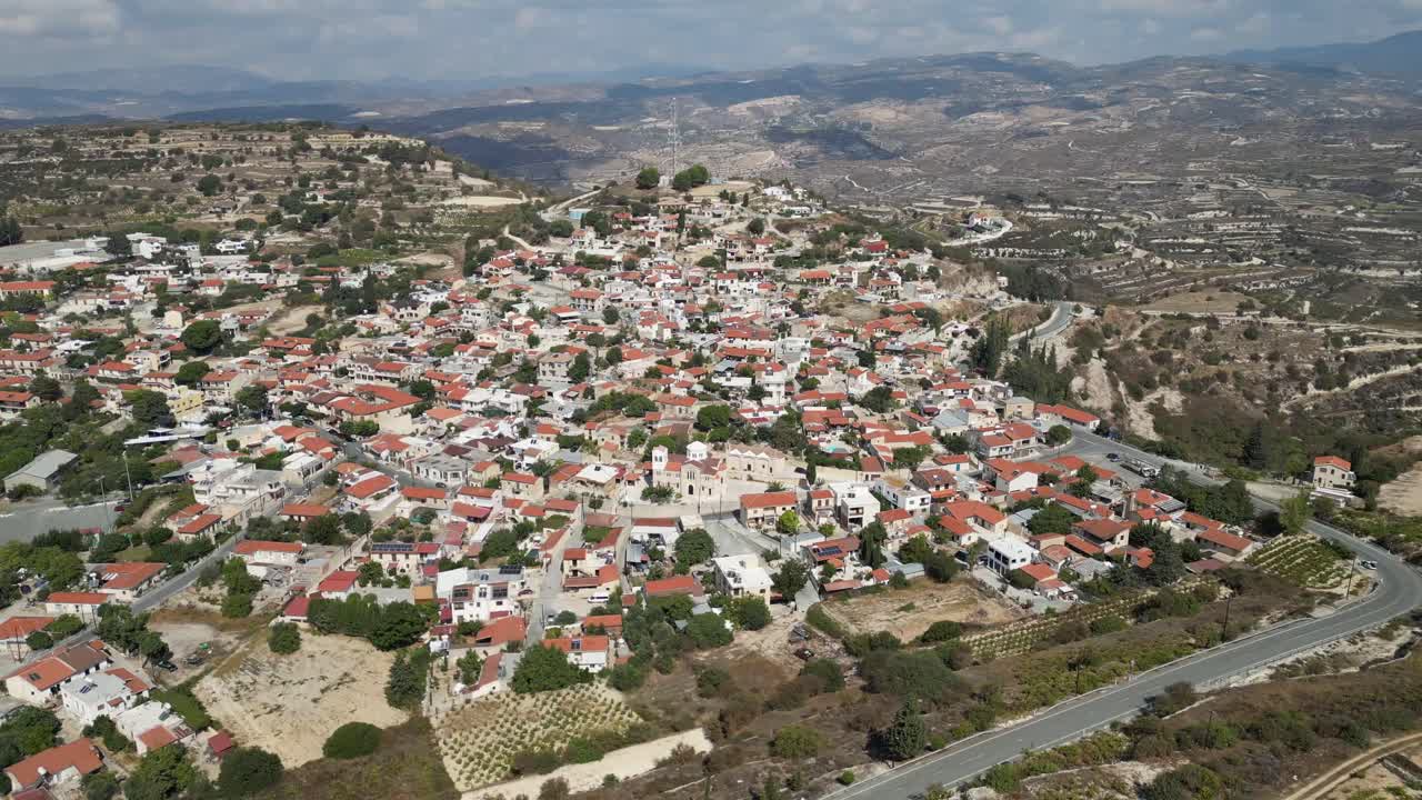 Cinematic drone aerial view of a sprawling village with winding roads intersecting at various angles, showcasing charming red-roofed houses across the landscape.