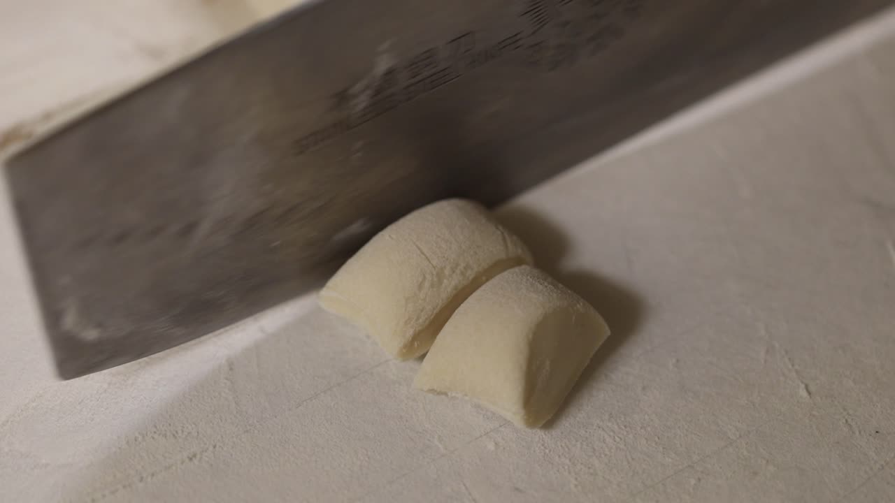 el chef corta con cuidado un rollo de masa con un cuchillo de cocina grande