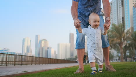 Young-father-with-a-child-and-first-steps.-Young-father-with-a-child-at-outdoor-learninig-for-a-first-steps-near-urban-house-in-the-city