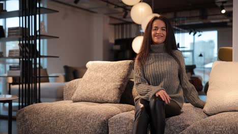 a Beautiful Woman in a Gray Sweater is Sitting on a Sofa in a Furniture Store a Beautiful Woman in a Gray Sweater is Sitting on a Sofa in a Furniture Store High Quality Footage