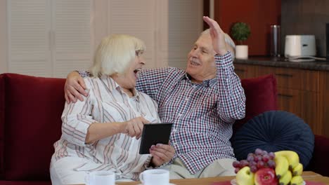 Senior-old-couple-grandparents-talking-and-using-digital-tablet-computer-at-home.-Internet-shopping