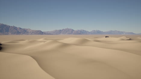 dunas de arena en un desierto con montañas en el fondo