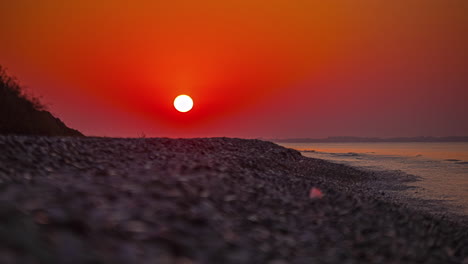 sunrise with the sun glowing bright over a pebble beach in cyprus - time lapse