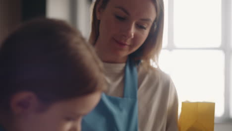 uma mulher bonita está a ver como a sua filha está a misturar a massa para o bolo. a mãe e a criança estão a cozinhar.