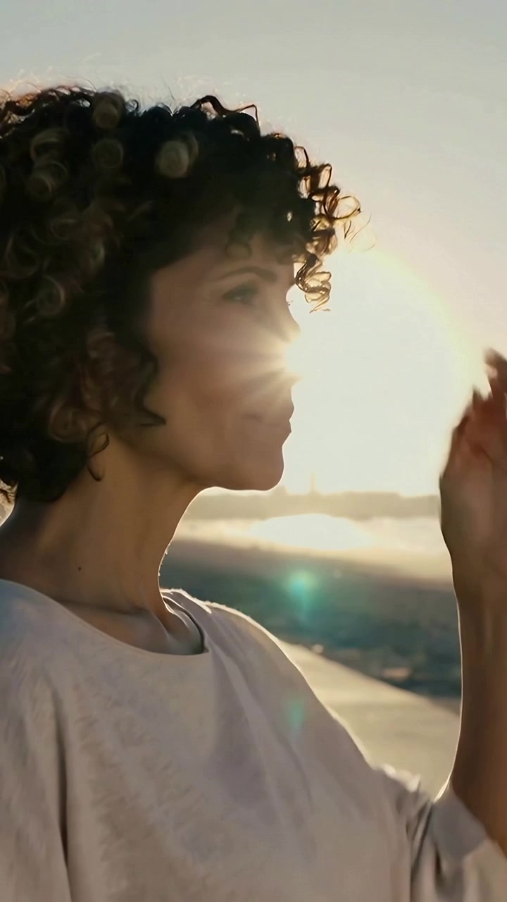 Vertical video: Reacting to sun, woman raising hand, shading eyes, tucking hair on seafront, flare