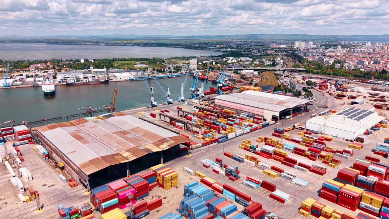 Burgas, Bulgária, 1 de maio de 2026: Contêineres de Carga e Guindastes em Porto Industrial. Vista aérea de pilhas de contêineres, guindastes portuários, armazéns, navios de carga, trilhos de trem e fundo da cidade.