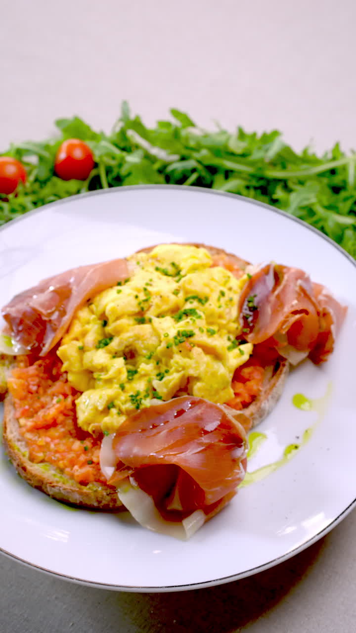 Eastern European cuisine presents scrambled eggs with smoked ham, parmesan and chives on toasted bread with tomato sauce, decorated with arugula and cherry tomatoes on a white background