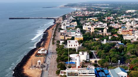 a detailed aerial shot captures the famous promenade beach and coastline of puducherry, india. the drone footage glides along the scenic coastal road, revealing a long pier