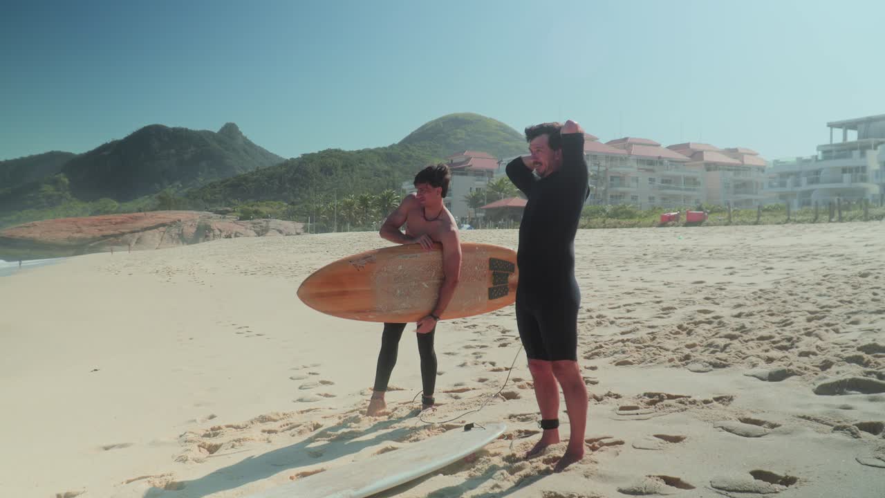 Two men on a sunny beach preparing to surf with their surfboards