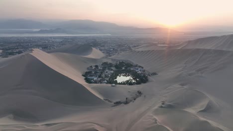 Oasis-Del-Desierto-Huacachina,-Perú-Con-Lago-Y-Palmeras,-Con-Grandes-Dunas-De-Arena-En-El-Fondo