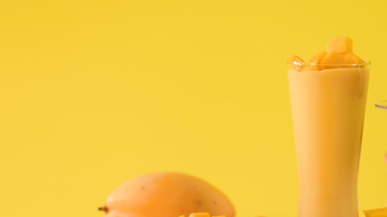 Luminosa foto in studio di un bicchiere di frullato al mango con frutta fresca, mano che aggiunge una guarnizione, telecamera statica