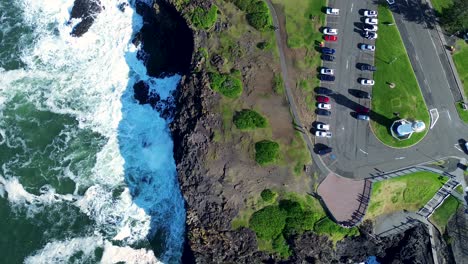 Landschaft-Aus-Der-Vogelperspektive-Auf-Die-Felsige-Landzunge-An-Der-Küste-Und-Den-Kiama-Blowhole-Parkplatz-Mit-Leuchtturm,-Geparkte-Autos,-Meer,-Hauptstraße-Der-Stadt,-Südküste,-Reisetourismus