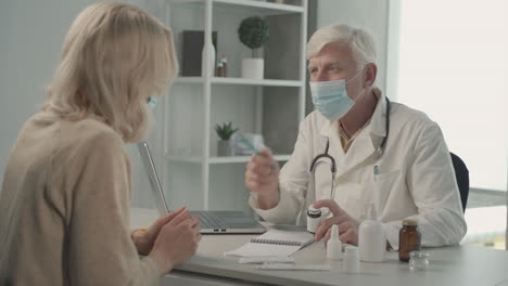 a grey haired, middle aged doctor in a facemask prescribes medicines to a female patient 2