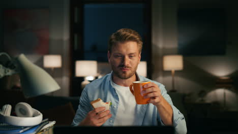 positive man videocalling home closeup. guy drinking taking sandwich break