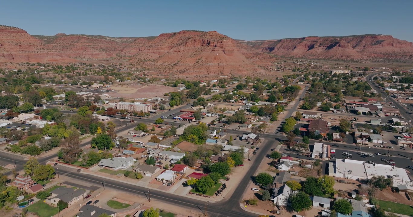 Vista aerea a media quota delle strade e delle case della città di Kanab, Utah, sotto scogliere desertiche di arenaria rossa.