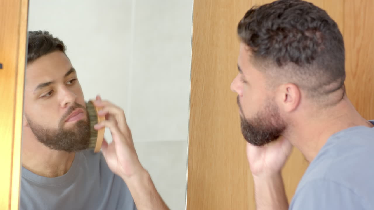 Grooming beard, man using brush and looking in mirror in bathroom