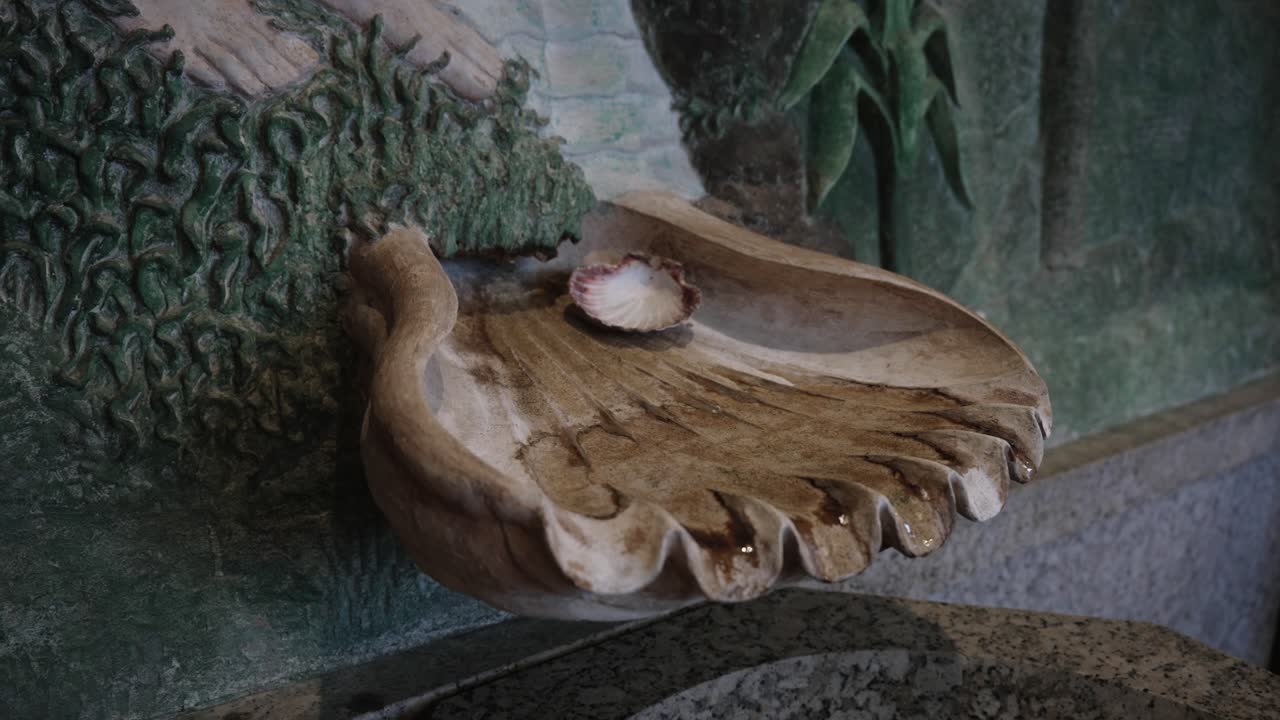 stone holy water font shaped like a hand with a scallop shell at the center