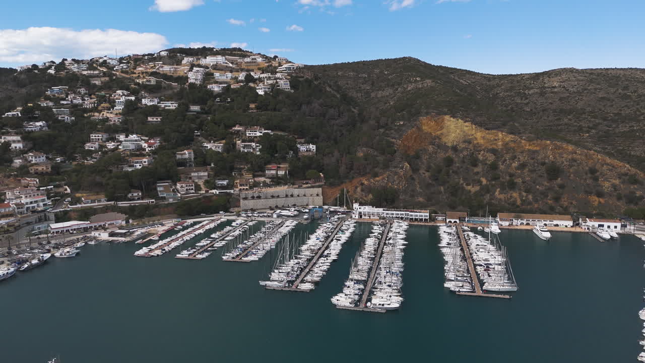 Slips packed with boats extend across marina beside curved coastline and forest
