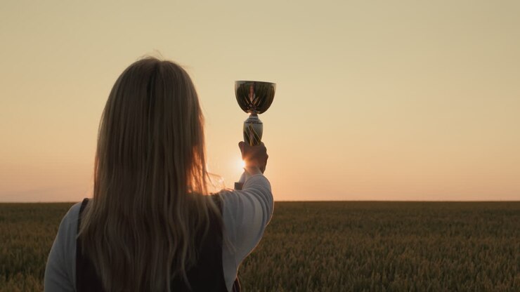 Contadina che solleva la coppa del campione in un campo di grano al tramonto.
