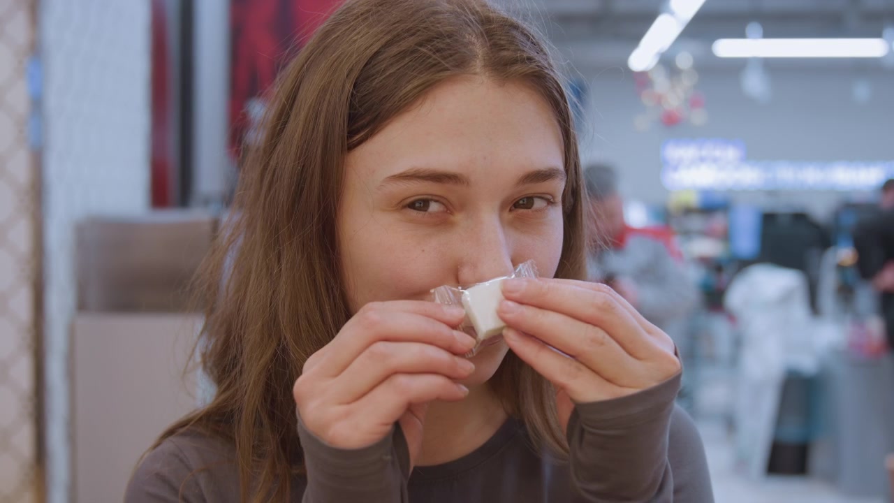Felice assaggio di dolci. Momento spontaneo catturato di una donna che si gode campioni di dolci al mercato. Scena luminosa che mostra una donna allegra che si gusta varie caramelle durante una vivace esperienza di shopping.