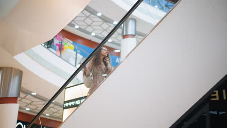 young woman in vintage dress ascending on escalator, adjusting her hair as she glances upwards, background features large display screen and modern architecture with lighting