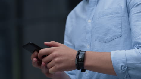 hombre de negocios usando un teléfono inteligente enviando mensajes de texto al aire libre. manos masculinas sostienen el dispositivo de cerca.