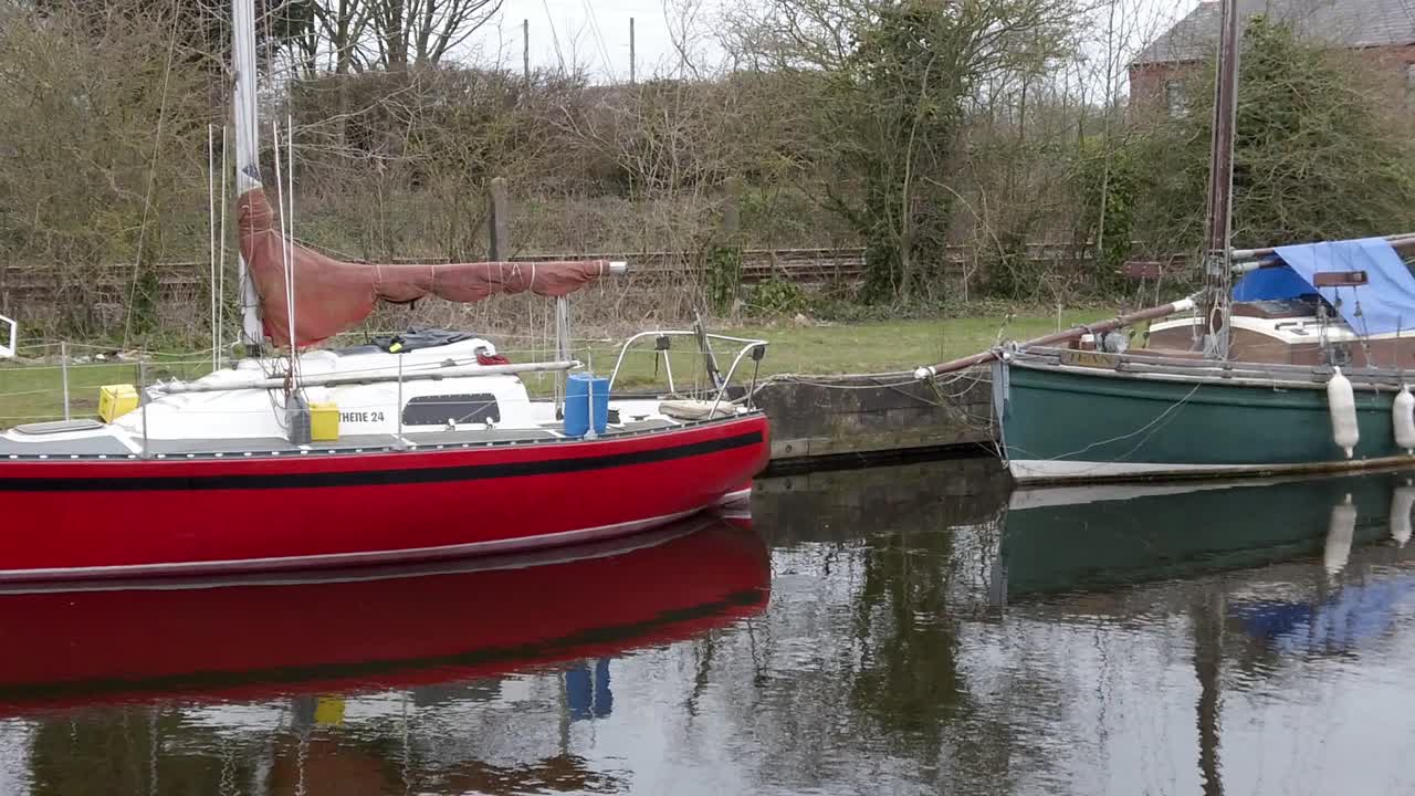 pequeños veleros rojos y verdes amarrados en un estrecho puerto deportivo de canal rural