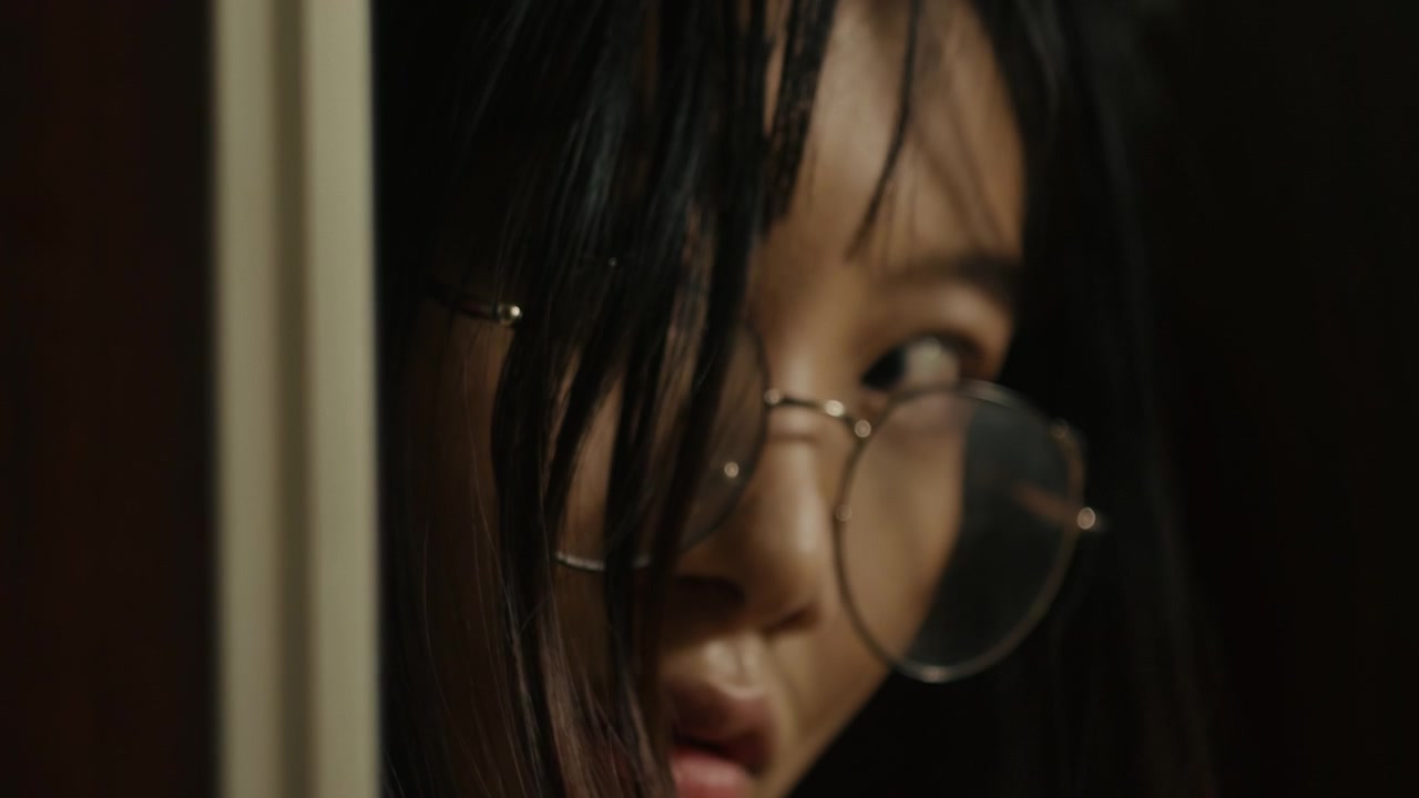 asiatic young girl with glasses opening a door, checking a room in the darkness. Nightmare of young woman that feels fear and scare.