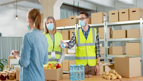 caucasian young male and senior female volunteers in facial mask giving food and water to homeless people in charity warehouse