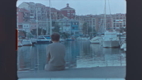 A person sits by a marina at dusk
