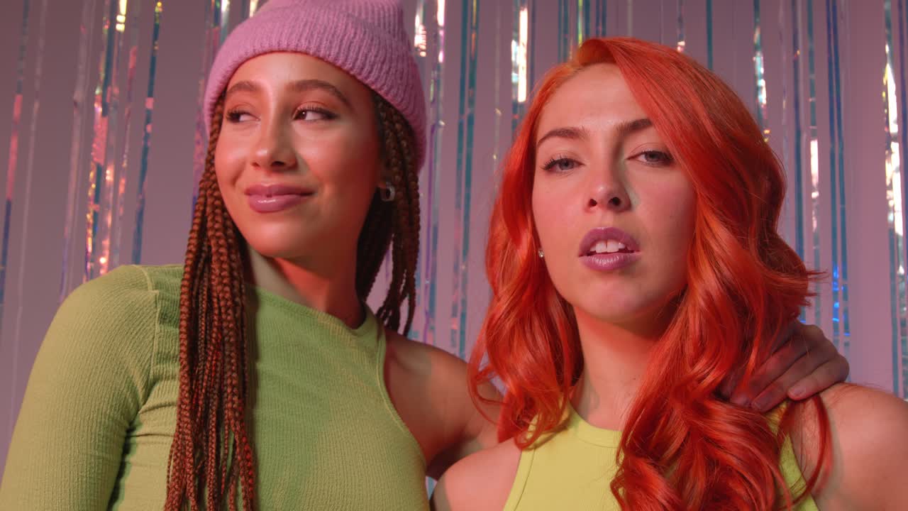 분홍색 배경에 tinsel 커튼 앞에 서있는 두 젊은 gen z 여성의 스튜디오 초상화