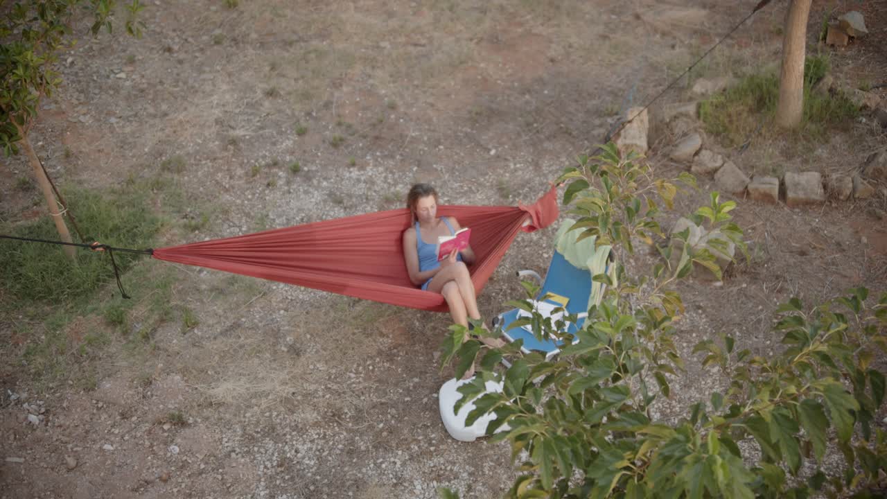 vista superior de una mujer solitaria feliz descansando en una hamaca leyendo un libro en el jardín