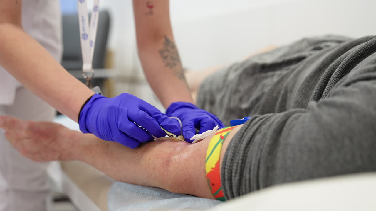 Gloved hands of a nurse input a needle into patient's vein. Taking blood test from a patient.