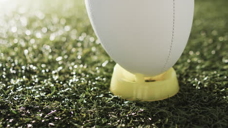 White-rugby-ball-on-kicking-tee-on-sunlit-grass-with-copy-space,-slow-motion