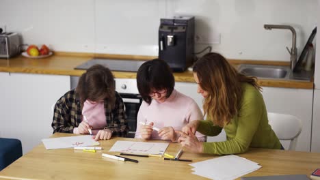 Zwei-Mädchen-Mit-Behinderung-Zeichnen-Gemeinsam-In-Der-Küche-Neben-Der-Lehrerin-Oder-Mutter