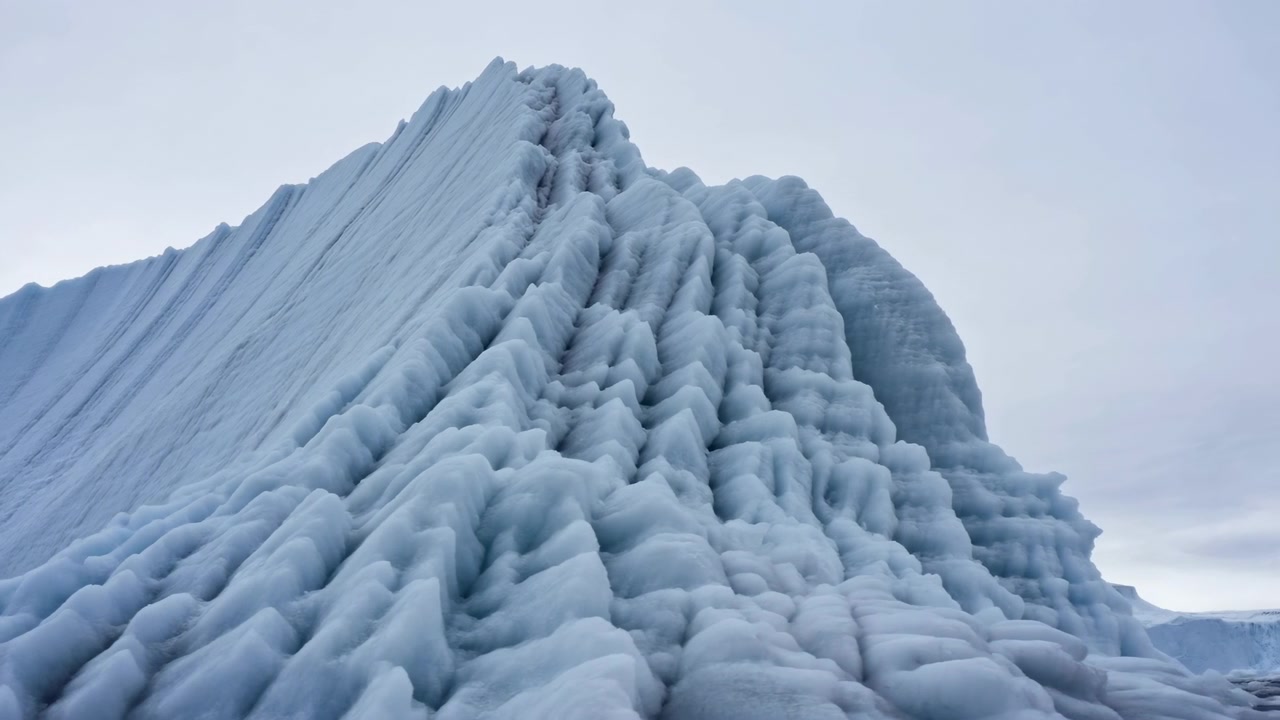 Inquadratura dal basso che mostra una cresta di ghiaccio glaciale scolpita con terrazze a gradoni, rigonfiamenti arrotondati, cresta affilata, superficie ghiacciata e texturizzata, sottili tonalità blu e luce soffusa e nuvolosa attraverso un paesaggio polare remoto