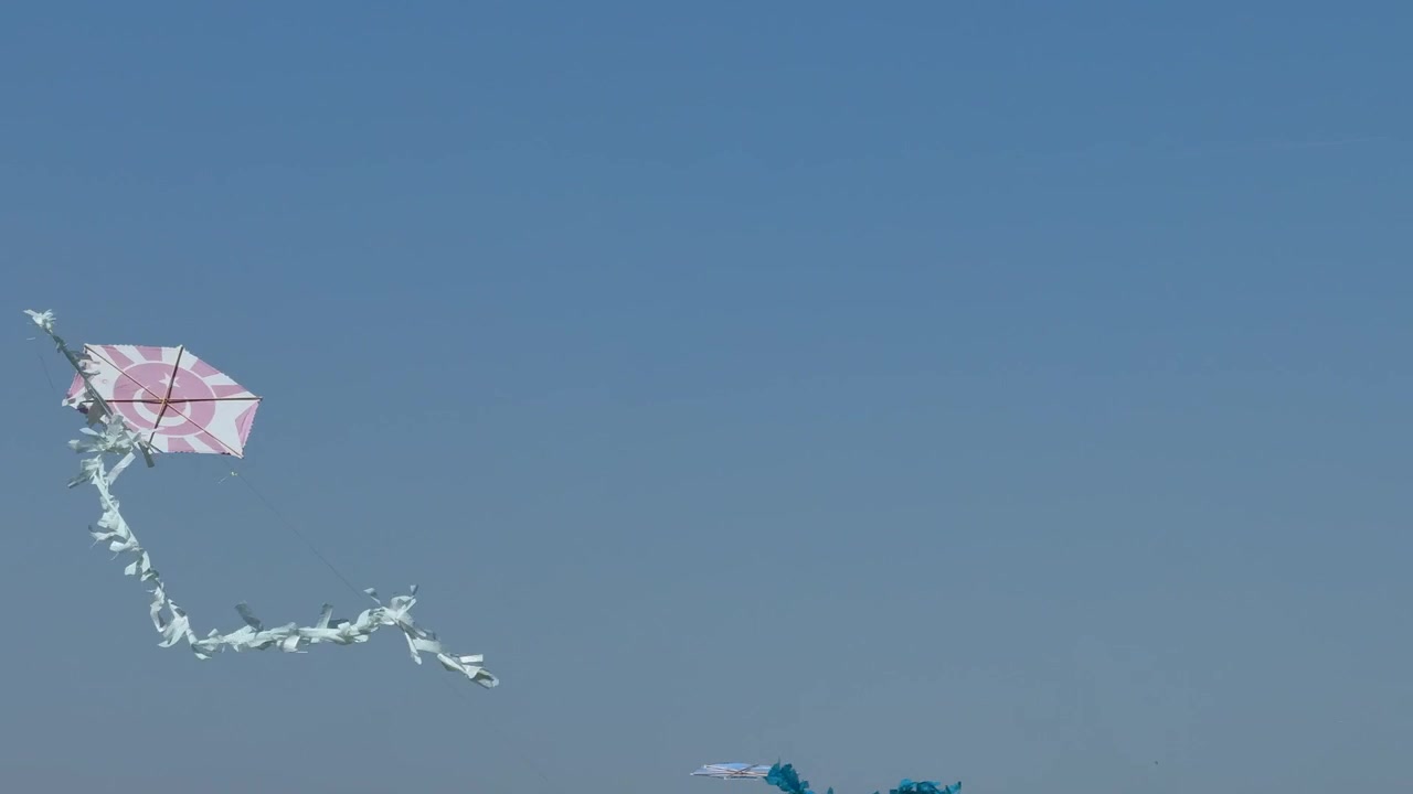 Una cometa clásica con una cola colorida volando con el viento en un cielo azul claro y sin nubes. Toma de naturaleza al aire libre de estilo minimalista con temática de libertad y diversión.
