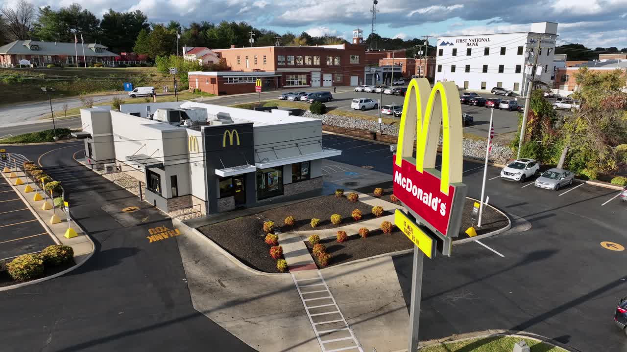 Aerial orbit shot of Mc Donalds Restaurant with sign and parking cars in america. Flag of USA and Bank in Background. Autumn day in suburb of american town. Virginia, America.