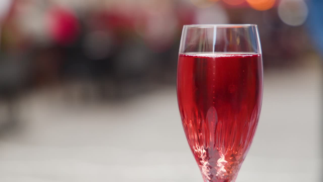 Crystal glass with red drink in sharp focus, blurred people and bokeh lights background
