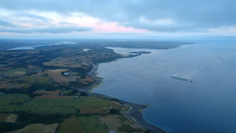 drone overview of rural fields and a aquaculture farm on the coastline of chiloe, gloomy evening