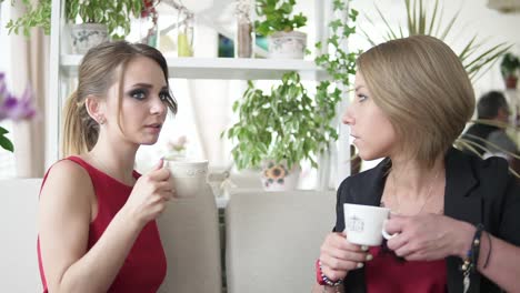 two attractive young women relaxing, talking and drinking coffee in coffee shot. slow motion shot