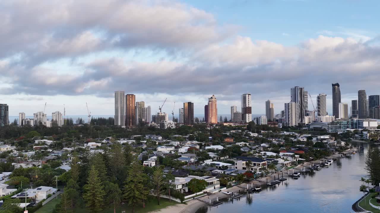 Drone pans across waterfront homes, canals, and city skyline under soft evening light, Gold Coast